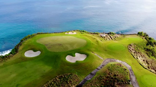 Aerial view luxury golf field next the cliff, ocean and beach in Bali island, Indonesia.  Aerial view of footpath on golf course.