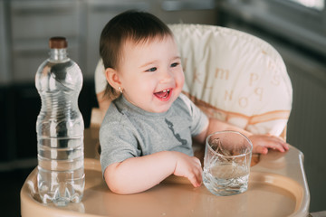 Cute little girl sitting in baby chair and drinking water