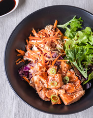 Top down view of donburi salmon with salad in black dish