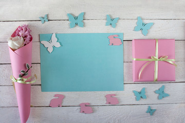 Wiosenne tło z niebieską kartą, prezentem przewiązanym wstążką,  kwiatami, motylami i zajączkami - obrazy, fototapety, plakaty