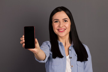 Closeup photo studio portrait of a pretty cute with a toothy smile holding a phone in hand device gadget wearing denim shirt isolated gray background copyspace