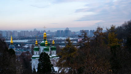 Fototapeta premium Golden domes of the church. Church in the trees. Church on the background of the city. Evening in the city. Church in winter