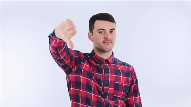 Disappointed young man showing thumb down gesture isolated over white background. Casual unsatisfied guy give dislike negative feedback as customer. Annoyance feeling.