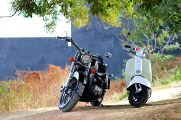 Vintage black motorcycle standing near white motorbike in rays of sunlight. Side view