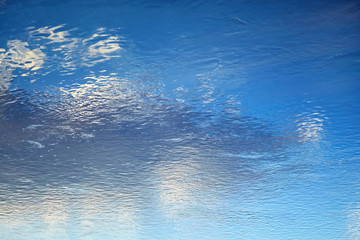 Reflection of blue sky and white clouds in the water. Ripples on the surface of the river. Abstract background