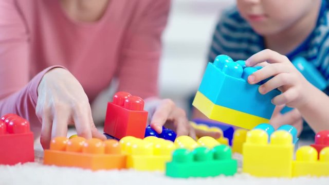 Close-up hands of female child psychologist and little boy playing with colored cubes during testing