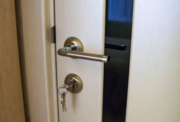 Metal door handle and keys close-up. white door with black glass