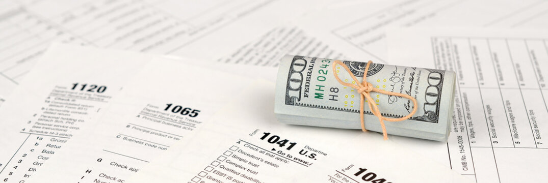Tax forms lies near roll of hundred dollar bills. Income tax return
