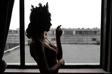 lateral view of a sexy fashion woman in pink underwear with crown on her head near a window