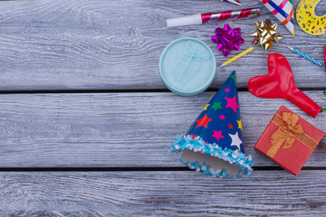 Birthday accessories on wooden background. Party hat, gift box, balloon, blowers and bows on wooden boards with text space.