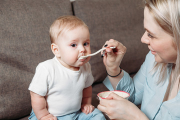 Happy mother nanny or sister feeds a little baby with a spoonful of food at home.