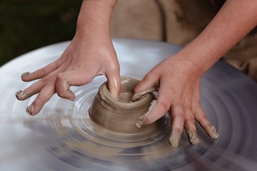Rotating potter's wheel and clay ware on it taken from above. A sculpts his hands with a clay cup on a potter's wheel. Hands in clay.