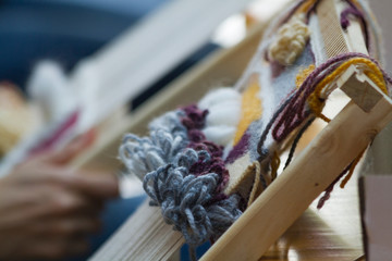 Tejido en telar vertical manos trabajando lana azul amarillo