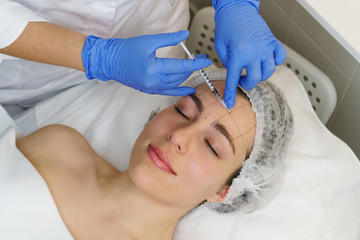 Aesthetic cosmetology. Hands of cosmetologist inject hyaluronic acid in forehead area of girl. Face lift. Correction of mimic wrinkles