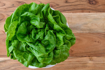 Head of fresh butter lettuce in a white bowl on a wood background