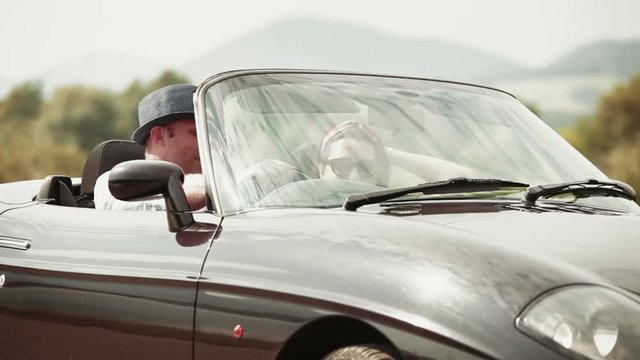 Couple cheerfully talking in convertible car, then setting off