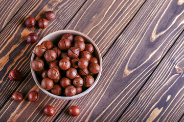 Macadamia nuts in a wooden bowl on a wooden background with copy space.