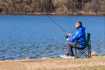 Fisherman catching fish in lakeside and sitting on chair. Man holding spinning