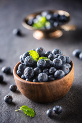 Wooden bowl full of fresh blueberries with herbs