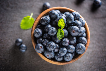 Wooden bowl full of fresh blueberries with herbs
