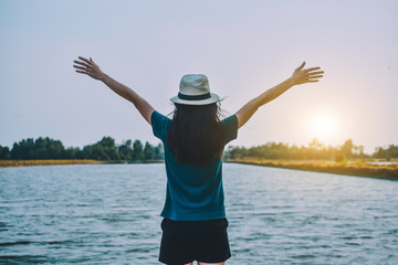 The woman wore a white T-shirt and a hat, standing on the river and the two hands on the sky.