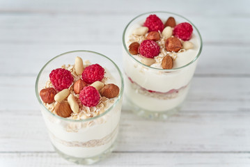 Two glasses of greek yogurt granola with raspberries, oatmeal flakes and nuts on a white background. Healthy nutrition