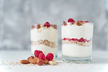 Two glasses of greek yogurt granola with raspberries, oatmeal flakes and nuts on a white background. Healthy nutrition