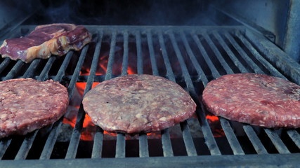 Three cutlets and steak on the grill close-up, in the background, coals roasted and smoke comes.