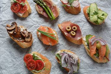 Brushetta or traditional Spanish-tapas. Appetizers with Italian antipasti snacks. Variety of small sandwiches with prosciutto,cherry tomatoes, salmon, cream cheese, cucumber, radish, asparagus