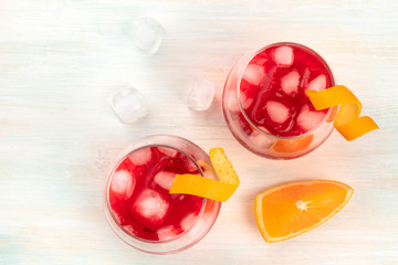 Cocktails with campari and orange curl garnishes, with ice cubes and an orange slice, shot from above with copy space
