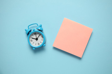 Blue alarm clock and a reminder note. Time management concept. Copy space for text.