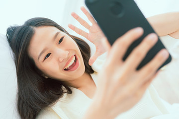 beautiful white shirt asian woman enjoy conversation hand hold smartphone on white bed holiday lifestyle