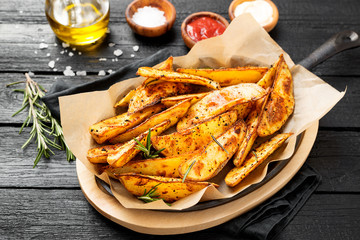Baked potato wedges with herbs and different sauce on black background.