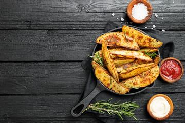 Baked potato wedges with herbs and different sauce on black background.