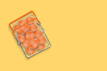One full glossy metal market basket of fresh raw brown eggs on yellow table on kitchen. Top view. Business concept. Copy space for your text