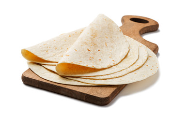 Homemade wheat flour tortilla on wooden cutting board isolated on white background.