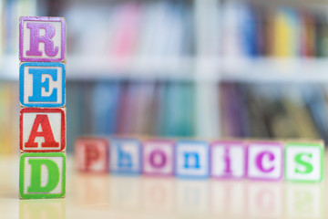 Alphabet blocks spelling the words read and phonics in front of a bookshelf - obrazy, fototapety, plakaty
