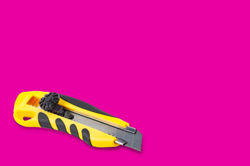Stationery knife with yellow and black plastic handle on pink background with copy space for your...