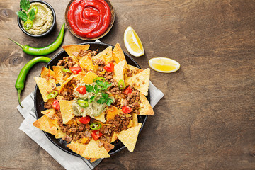 Corn chips nachos with fried minced meat and guacamole on wooden background.