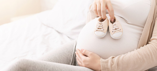 Small shoes for unborn baby on belly of pregnant woman