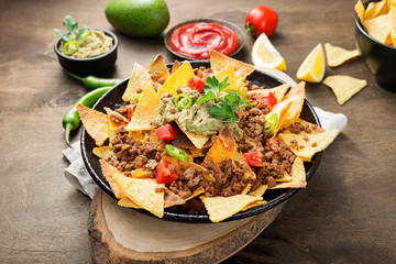 Corn chips nachos with fried minced meat and guacamole on wooden background.