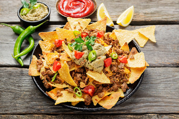 Corn chips nachos with fried minced meat and guacamole on wooden background.