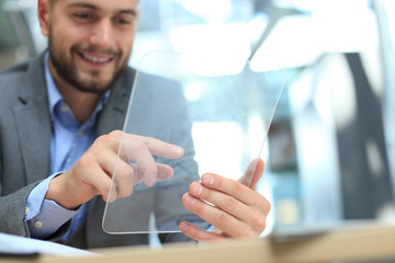 Businessman working in office with transparent tablet and laptop.