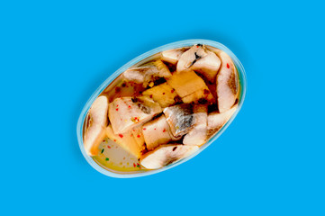 One oval transparent plastic container of canned seafood and spice in marinade in center on blue table on cuisine. Top view. Breakfast concept