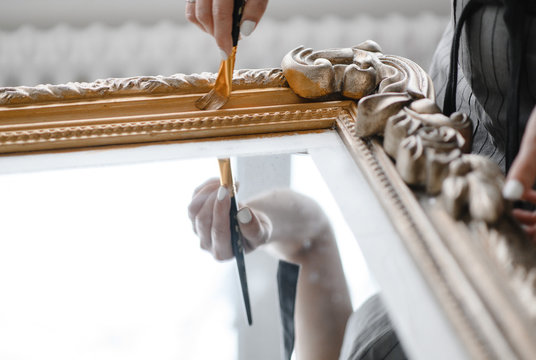 Young Girl Restores The Frame For The Mirror. Female Artisan Hands Working On A Big Wooden Picture Frame. Close Up