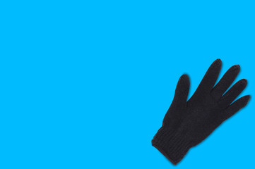 Black warm woolen glove on blue background with copy space for your text. Top view