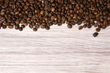 Roasted coffee beans in bulk on a light wooden background. dark cofee roasted grain flavor aroma cafe, natural coffe shop background, top view from above, copy space