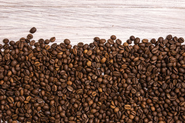 Roasted coffee beans in bulk on a light wooden background. dark cofee roasted grain flavor aroma cafe, natural coffe shop background, top view from above, copy space