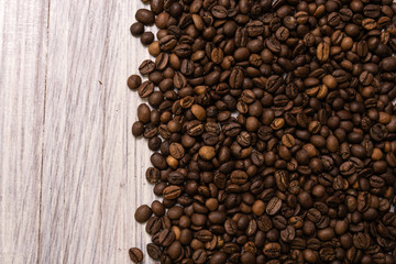 Roasted coffee beans in bulk on a light wooden background. dark cofee roasted grain flavor aroma cafe, natural coffe shop background, top view from above, copy space