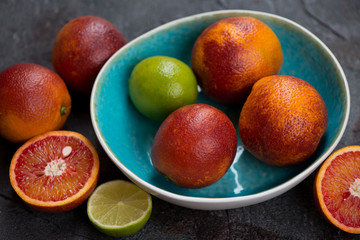 Whole and sliced blood oranges and limes in a turquoise bowl, studio shot, selective focus